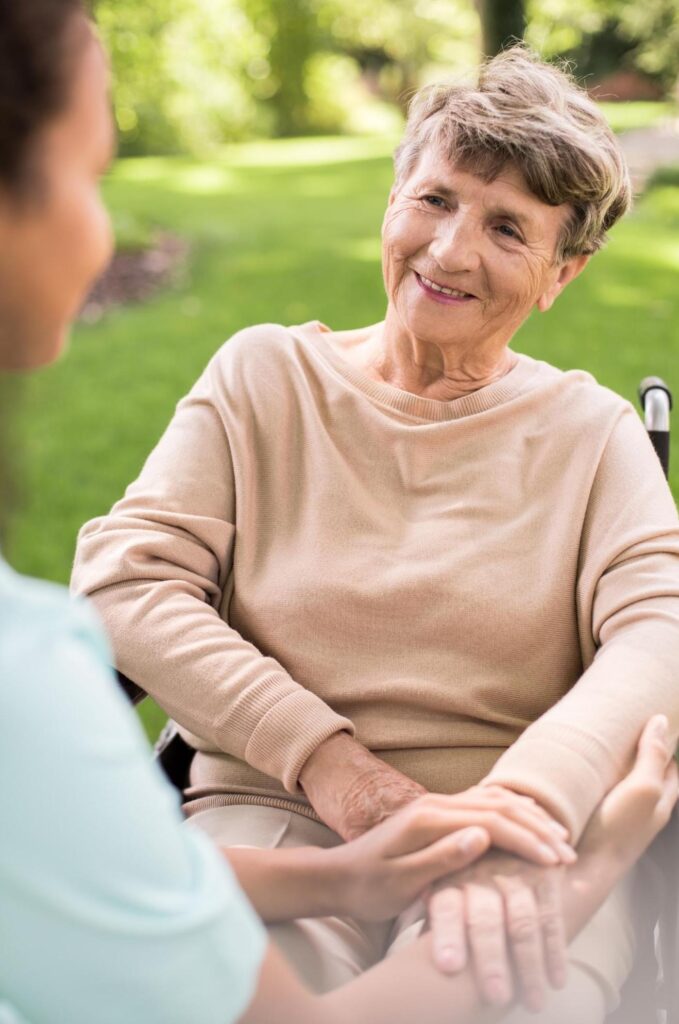 Elderly disabled woman sitting in a wheelchair and smiling at her daily living support worker. 