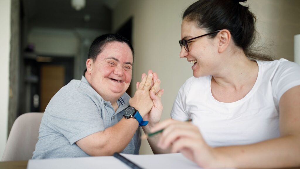 Disabled man high-fiving his in home disability support worker.